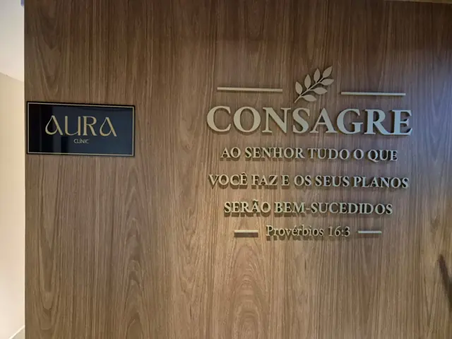 Entrada da Aura Clinic com placa dourada e painel de madeira